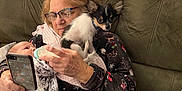 Roadrunner is registered to the contest to win money with this photo: baby, blanket, bottle_feeding, chihuahua, couch, cozy, curious, dog, elderly_woman, family, feeding, glasses, holding, home, indoor, pajamas, pet, portrait, sitting, smartphone