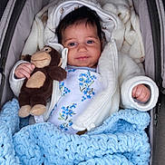 Eliza is registered to the contest to win money with this photo: baby, child, plush_toy, monkey, blanket, blue, white_jacket, floral_onesie, smile, cute, infant, soft_toy, cozy, portrait, indoors, hand, face, happy, warm, snug