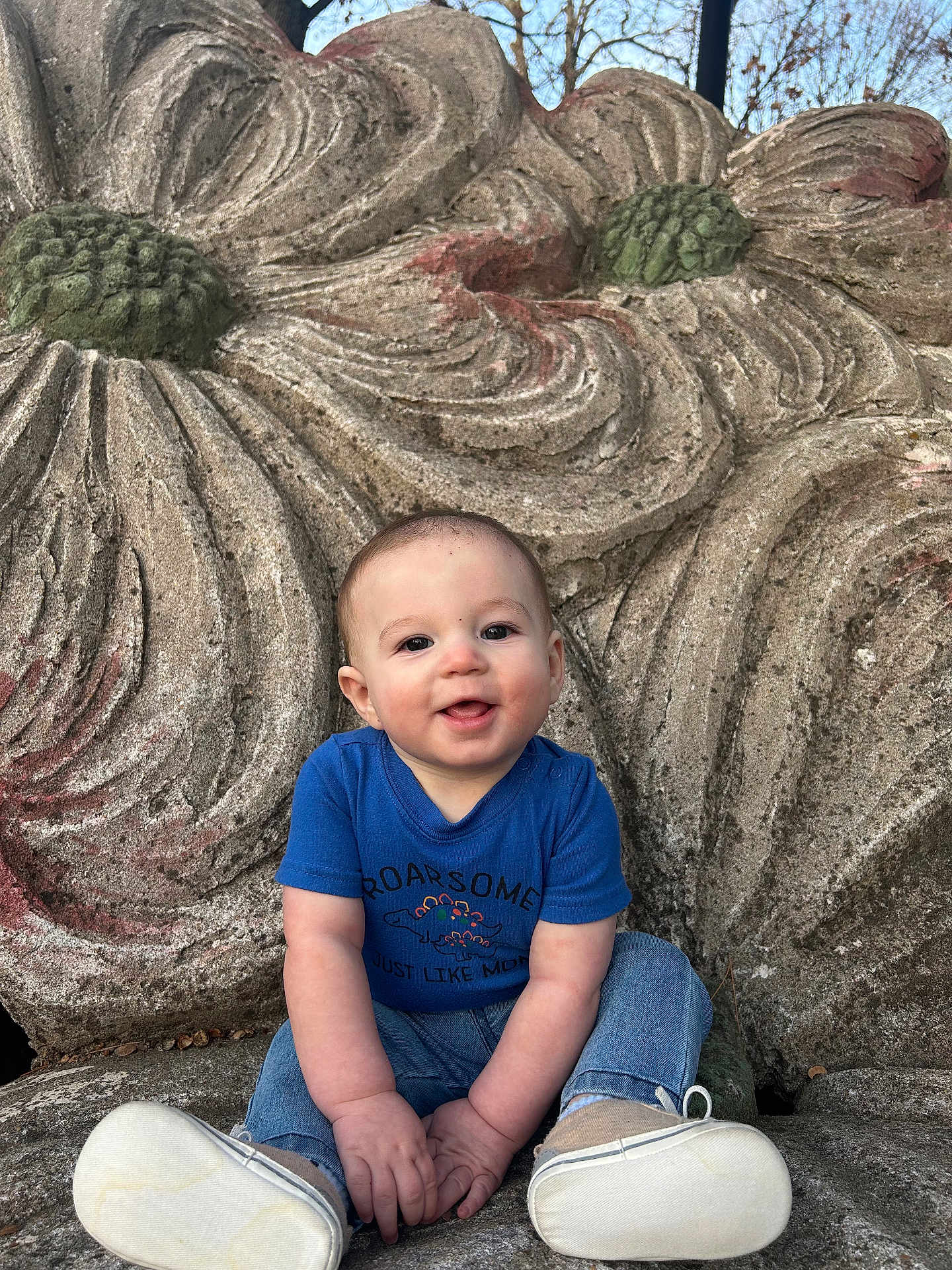 Zane is registered to the contest to win money with this photo: baby, child, smiling, blue_shirt, jeans, white_shoes, stone, carving, flower_pattern, outdoor, nature, portrait, cute, happy, playful, sitting, hands, face, head, daylight