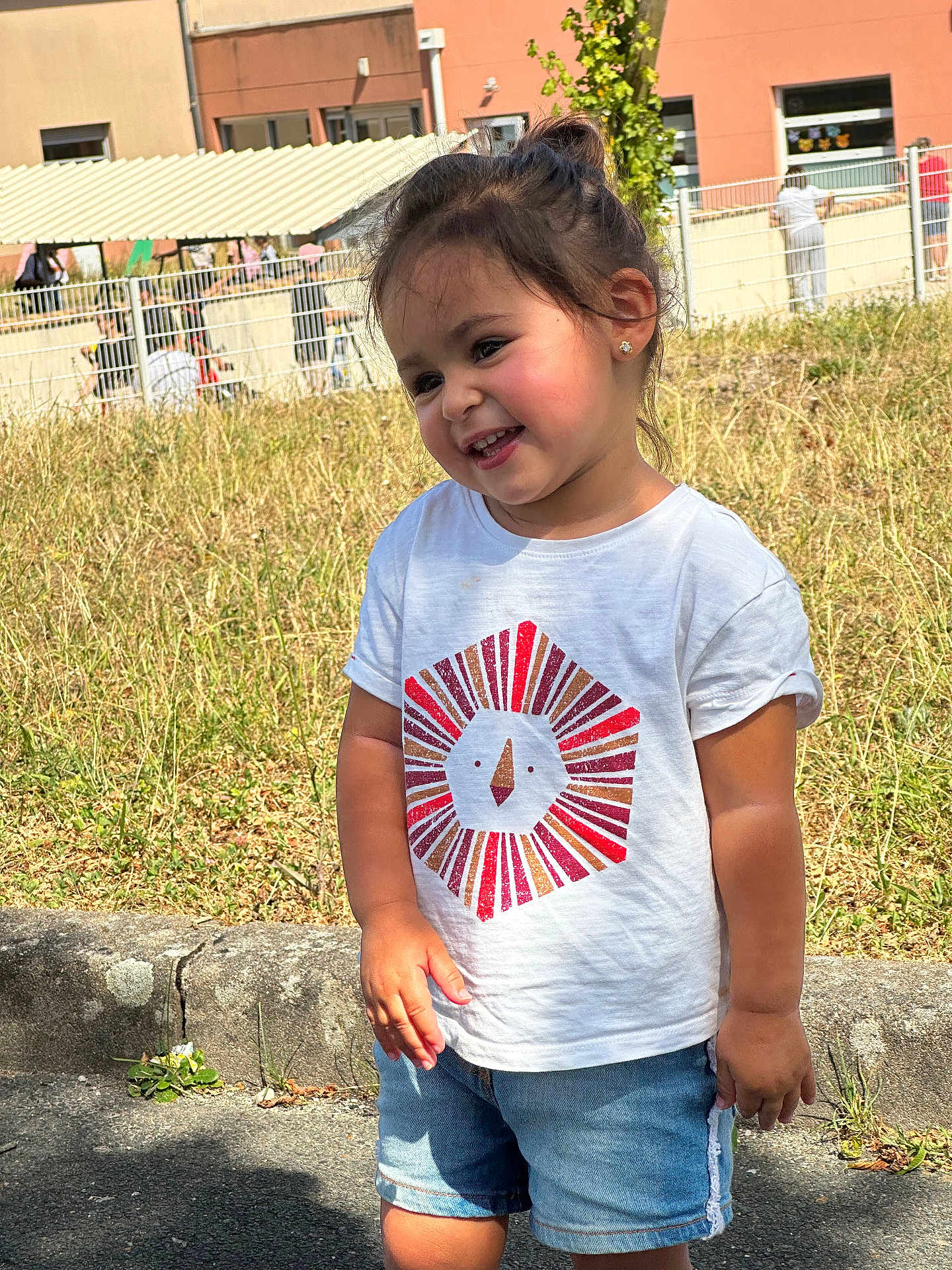 Dounia a rejoint le concours — aidez-le/la à gagner de superbes lots ! toddler, child, smiling, outdoor, grass, white_tshirt, denim_shorts, sunlight, fence, building, happy, cute, portrait, standing, casual_clothing, shorts, daylight, nature, playful, young_child