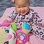 baby, child, pink, headband, bow, onesie, leopard_print, plush_toy, musical_toy, smiling, face, indoor, blanket, soft, happy, cute, infant, toy, colorful, sitting