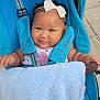 Janiyah is registered to the contest to win money with this photo: baby, child, stroller, blue_blanket, headband, bow, pacifier, smiling, outdoor, curly_hair, sitting, baby_clothing, safety_strap, happy, infant, person, cute, daylight, sidewalk, portrait