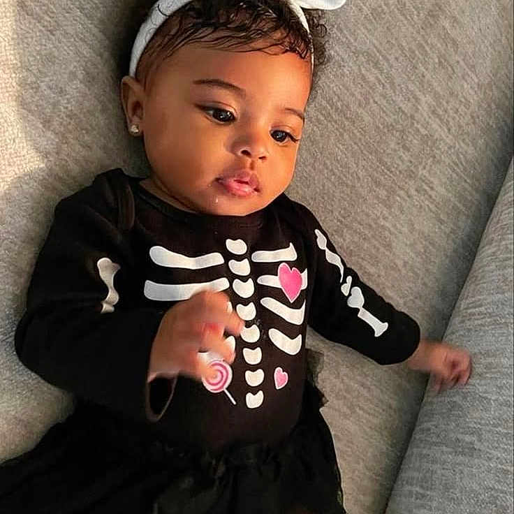 Jay'Lee is registered to the contest to win money with this photo: baby, black_clothing, bow, child, closeup, couch, curious, cute, earrings, girl, gray_couch, headband, indoors, infant, lollipop, pink_hearts, portrait, skeleton_outfit, smiling, tutu_skirt