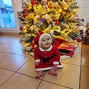Luna participe au concours pour gagner de l'argent avec cette photo : baby, celebration, child, christmas_tree, cute, decoration, festive, floor, happy, holiday, indoors, lights, ornaments, present_box, red_dress, santa_hat, seasonal, smiling, tiled_floor, winter