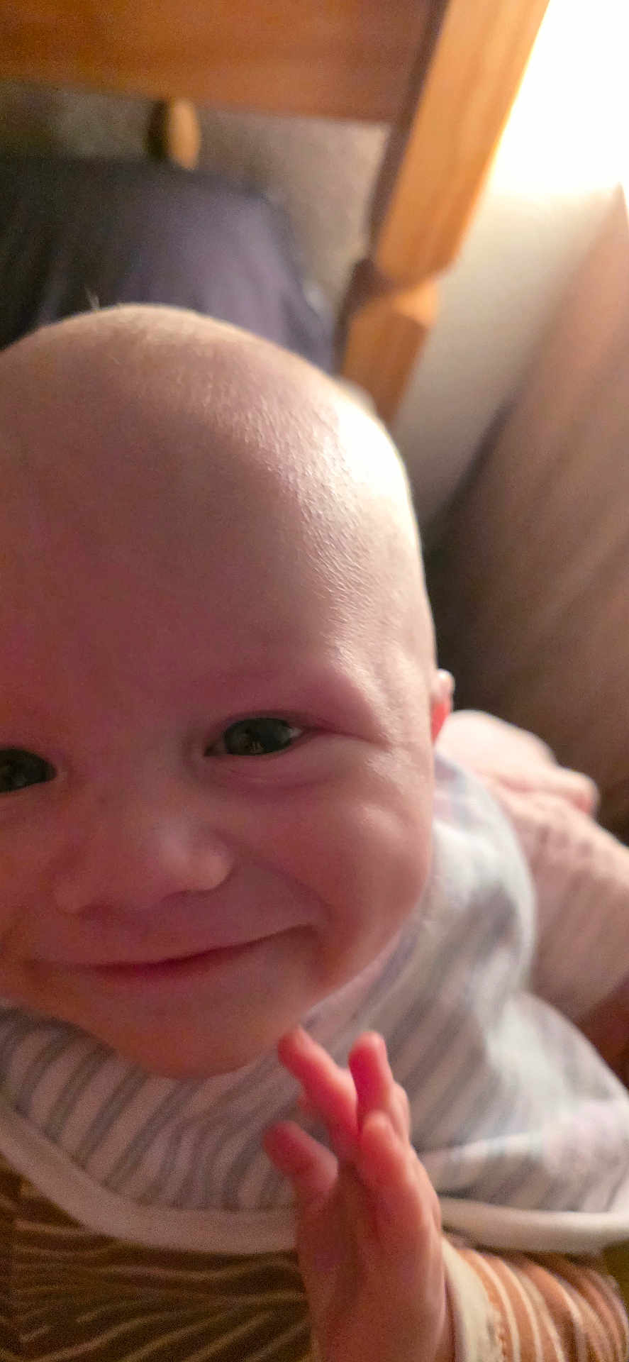 Archie is registered to the contest to win money with this photo: baby, smiling, close_up, face, hand, bib, striped_clothing, infant, cute, indoors, child, portrait, happy, young, skin, person, head, expression, newborn, soft_lighting