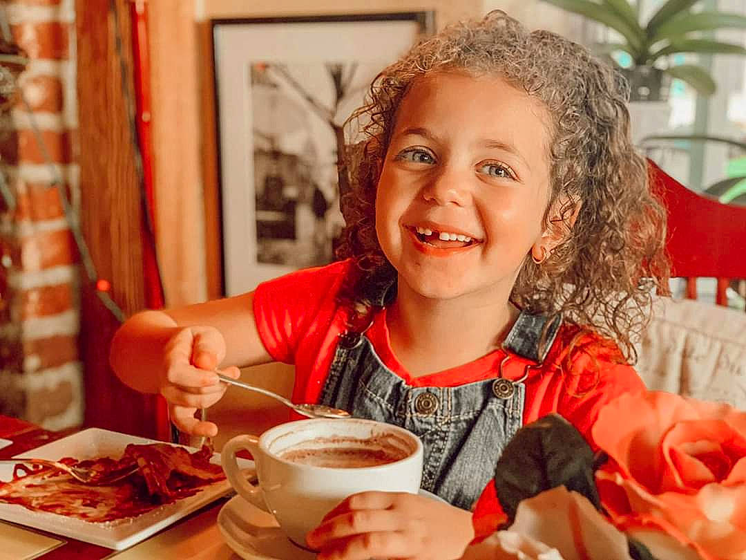 Sophie a rejoint le concours — aidez-le/la à gagner de superbes lots ! breakfast, brunch, child, coffee_cup, cuisine, dish, eating, facial_expression, fast_food, food, happy, joy, lunch, meal, person, saucer, serveware, sitting, smile, tableware
