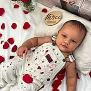 Elias is registered to the contest to win money with this photo: baby, infant, rose_petals, roses, vase, milestone_plaque, three_months, blanket, overalls, white_overalls, pillow, newspaper_background, portrait, lying_down, baby_face, hand, soft_lighting, celebration, cute, studio_shot