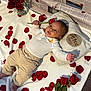 Elias is registered to the contest to win money with this photo: baby, infant, newborn, rose, rose_petals, bouquet, vase, pillow, blanket, milestone_card, newspaper_background, onesie, pants, feet, hand, face, portrait, laying_down, red_rose, cute