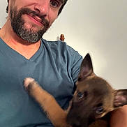 Cookie participe au concours pour gagner de l'argent avec cette photo : beard, blue_shirt, blur, brown_dog, candid, casual, close_up, dog, face, holding, human, indoor, interaction, man, pet, playful, portrait, puppy, smile, young_dog