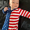 Hunter is registered to the contest to win money with this photo: baby, background, blue, child, curious, cute, face, hand, infant, lying_down, onesie, patterned_clothing, person, portrait, red, skin, sleepwear, stars, stripes, white