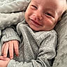 baby, smile, face, hand, blanket, gray_clothing, cozy, infant, portrait, cute, soft_texture, close_up, happy, child, skin, newborn, resting, warm, comfort, expression