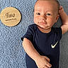 baby, infant, newborn, blue_blanket, wooden_plaque, two_months, onesie, navy_blue, nike_logo, face, arm, hand, lying_down, milestone, cute, portrait, skin, expression, indoor, soft_texture