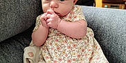 Maddie is registered to the contest to win money with this photo: baby, child, girl, floral_dress, headband, bow, couch, blanket, socks, indoors, cute, portrait, infant, seated, soft_lighting, cozy, hands, looking, curious, comfortable
