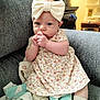 baby, child, girl, floral_dress, headband, bow, couch, blanket, socks, indoors, cute, portrait, infant, seated, soft_lighting, cozy, hands, looking, curious, comfortable