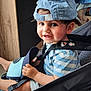 toddler, child, smiling, cap, blue_cap, striped_shirt, stroller, indoor, furniture, window, curtains, shelf, toy, happy, seated, person, face, baby, clothing, footwear