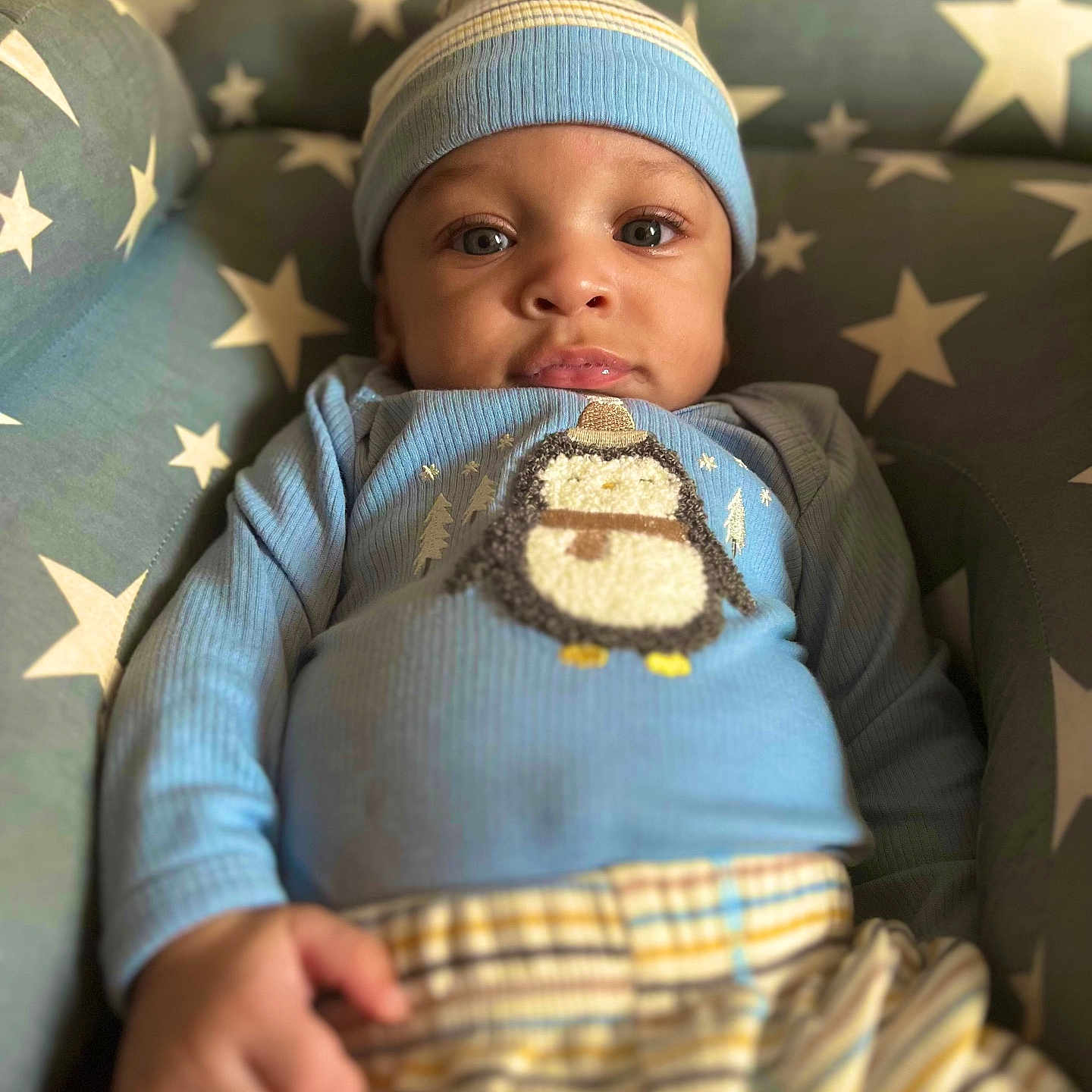 Atorion Jones is registered to the contest to win money with this photo: baby, blue_clothing, child, cozy, cushion, cute, face, hand, hat, headwear, indoors, infant, lying_down, penguin_design, portrait, relaxed, smiling, soft_fabric, star_pattern, striped_pants