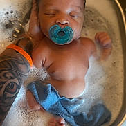 Atorion Jones is registered to the contest to win money with this photo: adult_hand, baby, bath, blue_cloth, blue_pacifier, bubble_bath, bubbles, closeup, foot, hand, infant, pacifier, peaceful, sink, skin, sleeping, soapy_water, tattoo, tattooed_arm, water