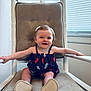 baby, child, smiling, rocking_chair, cushion, dress, hair_clip, indoor, window_blinds, arms_outstretched, footwear, happy, person, infant, seat, furniture, light, portrait, young_child, comfortable