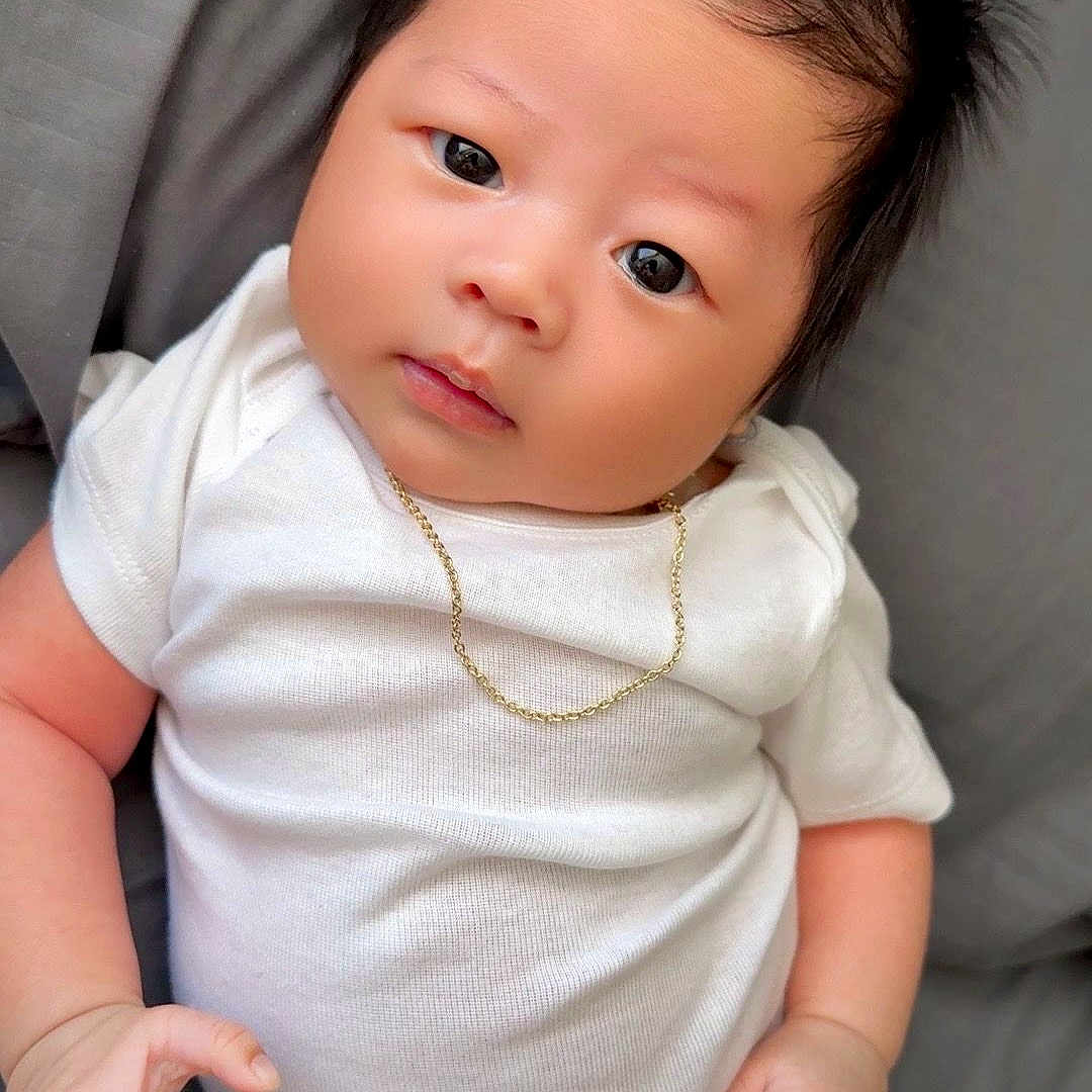 Daren joined the competition — help win amazing prizes! baby, infant, child, white_onesie, gold_chain, spiky_hair, cute, portrait, lying_down, soft_surface, skin, hand, face, expression, newborn, adorable, young, indoors, person, closeup