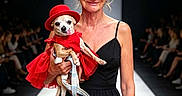 Margarita Olive is registered to the contest to win money with this photo: woman, dog, dress, red_hat, runway, fashion, audience, black_dress, pet, cute, portrait, smile, event, indoor, leash, small_dog, model, holding, catwalk, lighting
