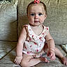 baby, child, infant, blue_eyes, pink_bow, strawberry_pattern, couch, beige, clothing, sitting, portrait, indoor, cute, skin, face, hand, foot, hair, expression, young