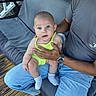 adult, baby, blue_eyes, blue_jeans, brick_wall, child, expression, footwear, gray_tshirt, green_outfit, hand, holding, outdoor, person, porch, sitting, sock, swing, watch, wooden_floor