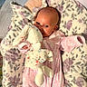 baby, blanket, bunny, carpet, child, cozy, cute, flooring, floral_pattern, head, indoor, infant, laying_down, person, pink_clothing, plush_toy, portrait, smiling, soft_toy, young_child