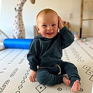 Austin joined the competition — help win amazing prizes! baby, child, smiling, sitting, indoors, playmat, toy, giraffe_toy, feet, hand, face, clothing, hoodie, pants, floor, pattern, playroom, happy, cute, infant