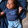 baby, infant, child, portrait, smiling, wide_eyed, lying_down, blanket, navy_blue, clothing, onesie, shirt, pants, star_pattern, couch, indoor, cozy, raised_hand, dark_skin, close_up