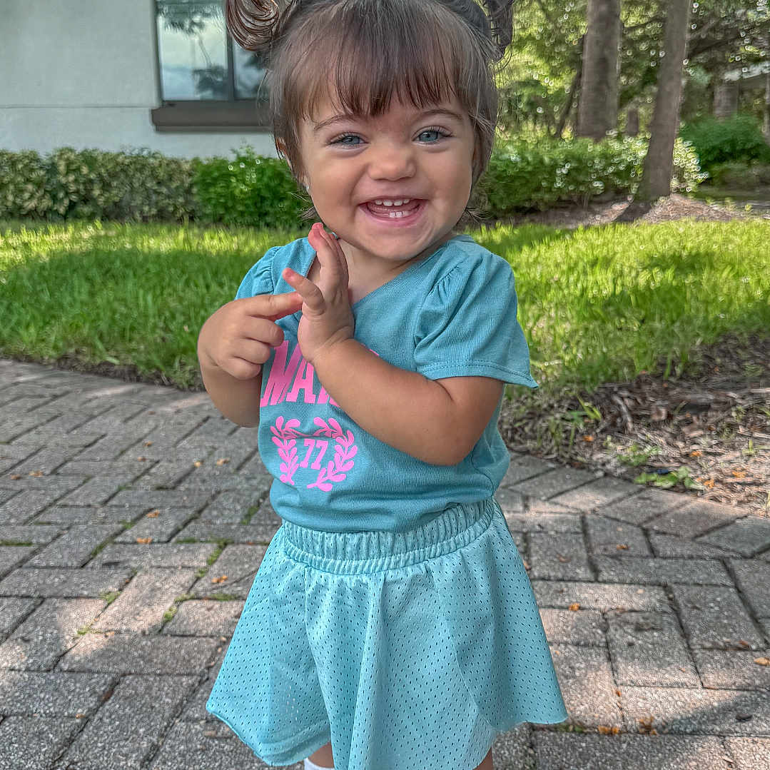 Bella joined the competition — help win amazing prizes! blue_clothing, building, casual_wear, child, cute, daylight, grass, happy, nature, outdoor, person, pigtails, portrait, sidewalk, smiling, sunlight, toddler, tree, white_shoes, young_child