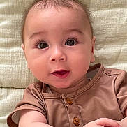 Logan participe au concours pour gagner de l'argent avec cette photo : baby, blanket, brown_shirt, child, close_up, curly_hair, cute, expression, eyes, face, hands, infant, lying_down, natural_light, person, portrait, skin, smile, soft_texture, wooden_buttons