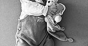Logan participe au concours pour gagner de l'argent avec cette photo : baby, black_and_white, child, couch, cute, fabric_texture, face, hands, indoor, infant, knitted_booties, monochrome, onesie, overalls, pacifier, peaceful, plush_toy, sleeping, soft_toy, teddy_bear