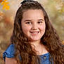 child, girl, smile, long_hair, curly_hair, blue_dress, portrait, face, necklace, autumn_leaves, background_blur, happy, person, outdoor, nature, fall_colors, young, casual_clothing, headshot, friendly
