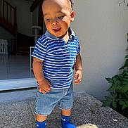 Issa a rejoint le concours — aidez-le/la à gagner de superbes lots ! toddler, child, boy, blue_shirt, striped_shirt, denim_shorts, blue_socks, outdoor, doorway, sunlight, smiling, happy, standing, casual_clothing, home_interior, plants, stairs, floor, portrait, playful