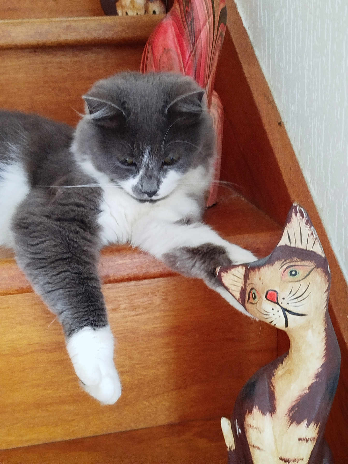 Alpha Saout participe au concours pour gagner de l'argent avec cette photo : cat, wooden_stairs, painted_cat_figure, gray_cat, white_paws, curious, indoor, pet, animal, feline, paw, wood, decor, resting, closeup, staircase, furniture, relaxed, playful, house