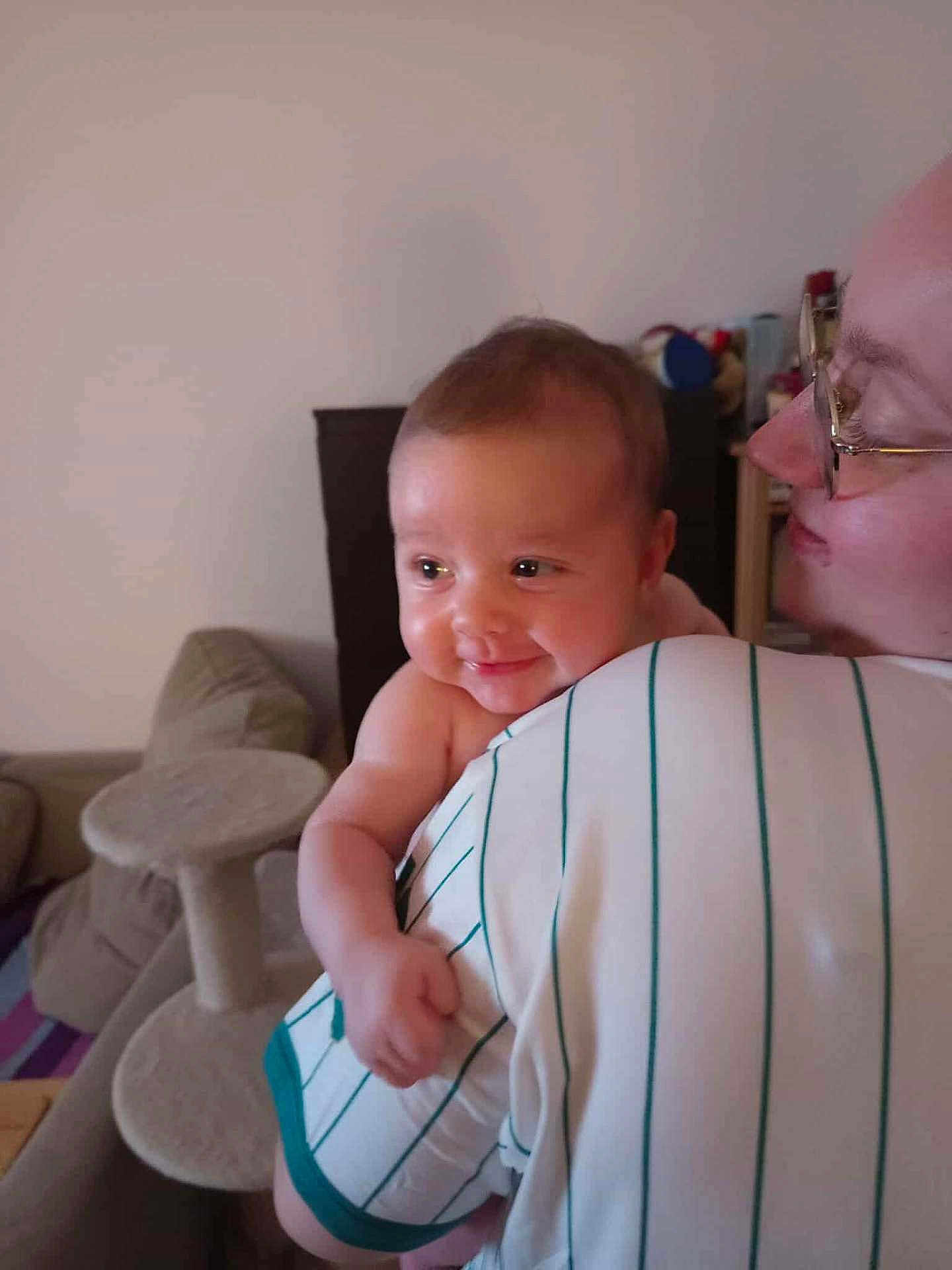 Armand participe au concours pour gagner de l'argent avec cette photo : baby, adult, person, smile, glasses, striped_shirt, indoor, living_room, furniture, couch, cat_tree, arm, head, face, holding, happy, closeup, skin, eyewear, child