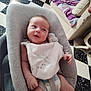 Armand a rejoint le concours — aidez-le/la à gagner de superbes lots ! baby, infant, smiling, bib, baby_chair, diaper, living_room, floor, checkered_floor, couch, blanket, pillow, child, person, indoor, happy, seat, clothing, furniture, cute