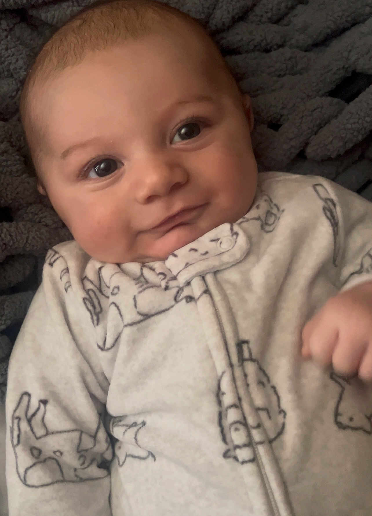 Lincoln is registered to the contest to win money with this photo: baby, infant, face, smile, onesie, clothing, animal_print, blanket, close_up, cute, child, portrait, soft_lighting, newborn, hand, skin, young, cozy, expression, lying_down