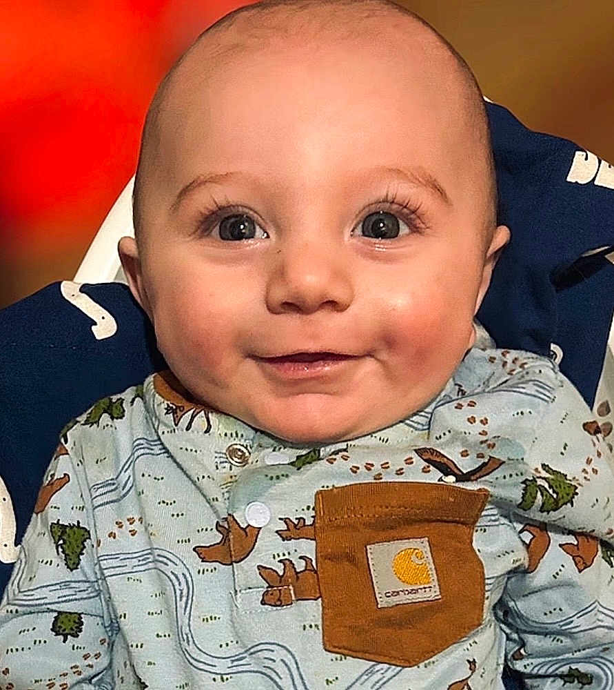 Lincoln is registered to the contest to win money with this photo: baby, infant, child, smile, big_eyes, eyelashes, dimples, bald_head, chubby_cheeks, onesie, patterned_clothing, chest_pocket, logo_patch, high_chair, indoor, portrait, close_up, cute, happy, soft_lighting