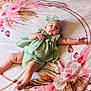 baby, infant, child, green_outfit, headband, blanket, floral_pattern, lying_down, cute, chubby_legs, pouty_face, reaching_hand, soft_texture, indoors, comfortable, relaxed, skin, expression, adorable, young