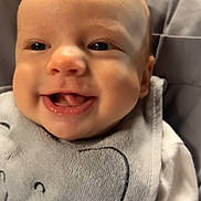 Taylor is registered to the contest to win money with this photo: baby, bib, cheeks, child, close_up, clothing, cute, elephant_design, eyes, face, happy, head, indoors, infant, mouth, newborn, person, skin, smile, tongue