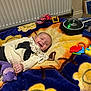 baby, blanket, smiling, toy, stuffed_animal, indoor, radiator, colorful, playtime, child, clothing, purple, yellow, orange, blue, black, plastic, happy, person, floor