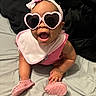 baby, child, pink_sunglasses, headband, smiling, crawling, pink_shoes, bib, indoors, bed, cute, happy, person, accessory, fashion, infant, portrait, closeup, fun, joyful