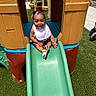 Brazille is registered to the contest to win money with this photo: toddler, child, slide, playground, outdoor, happy, smiling, toy_house, grass, summer, sunlight, sandals, bib, colorful, play, fun, young_child, daylight, park, recreation