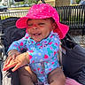 baby, child, stroller, pink_hat, strawberry_pattern, clothing, happy, smiling, outdoor, daylight, park, bench, tree, sunlight, skin, face, hands, infant, cute, sitting