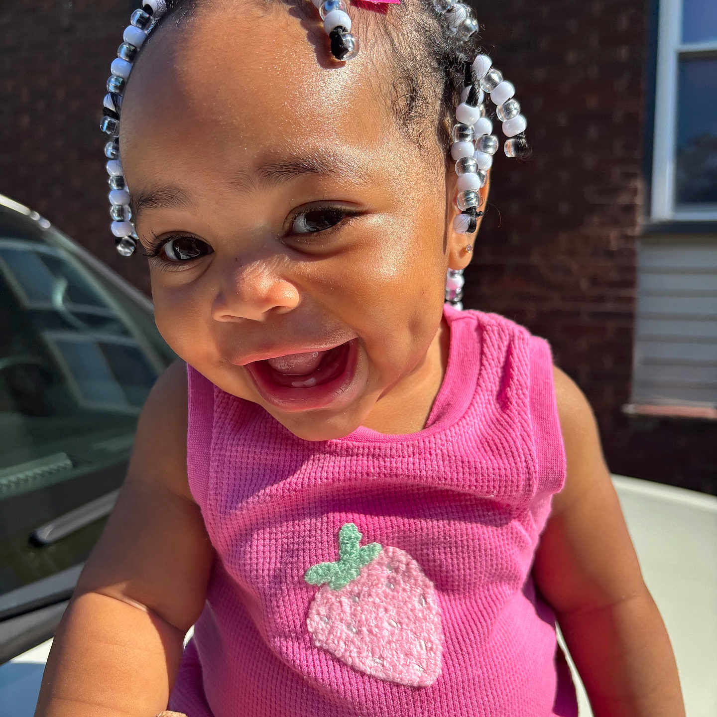 Brazille joined the competition — help win amazing prizes! toddler, child, smiling, happy, outdoor, beads, hair_accessories, pink_clothing, strawberry, cute, portrait, sunlight, face, person, baby, sitting, toy, window, car, brick_wall