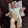 Anyelina Antonella is registered to the contest to win money with this photo: baby, child, infant, couch, pillow, headband, smile, clothing, plaid_pants, white_top, footwear, moccasins, indoor, person, cute, happy, reaching_hand, seated, soft_lighting, cozy