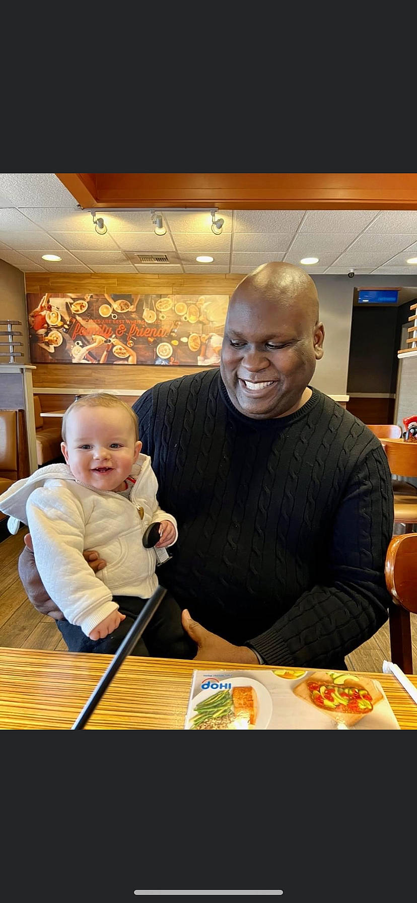 Beaux is registered to the contest to win money with this photo: baby, chair, child, cooking, customer, eating, event, fun, furniture, joy, orange, person, plate, recreation, sitting, smile, t_shirt, table, tableware, toddler