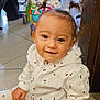 baby, cherry_pattern, child, cute, floor, furniture, happy, home, indoor, person, pigtails, playful, sitting, smiling, television, tile_floor, toddler, toy_walker, white_clothing, young_child