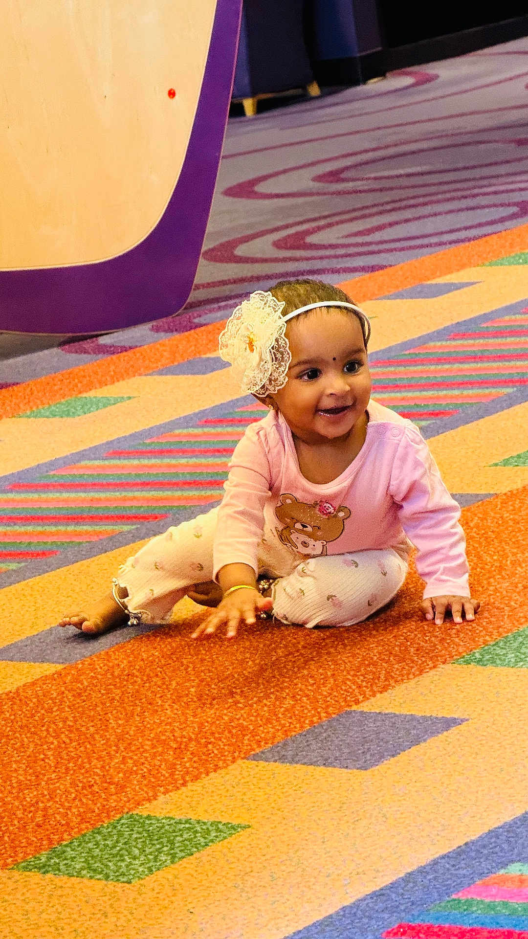 Aarna joined the competition — help win amazing prizes! child, baby, toddler, smiling, headband, flower_headband, pink_clothing, pants, bracelet, carpet, colorful, playful, sitting, portrait, indoors, happy, cheek, eyes, mouth, cute
